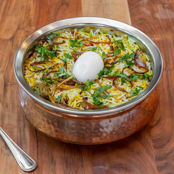Masthi Indian Cuisine's chicken biryani with a boiled egg, fried onions, and cilantro in a copper pot.