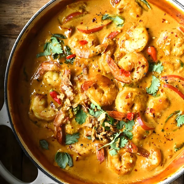 Close-up of a creamy orange Indian shrimp curry with red peppers, cilantro, and spices in a white pot.