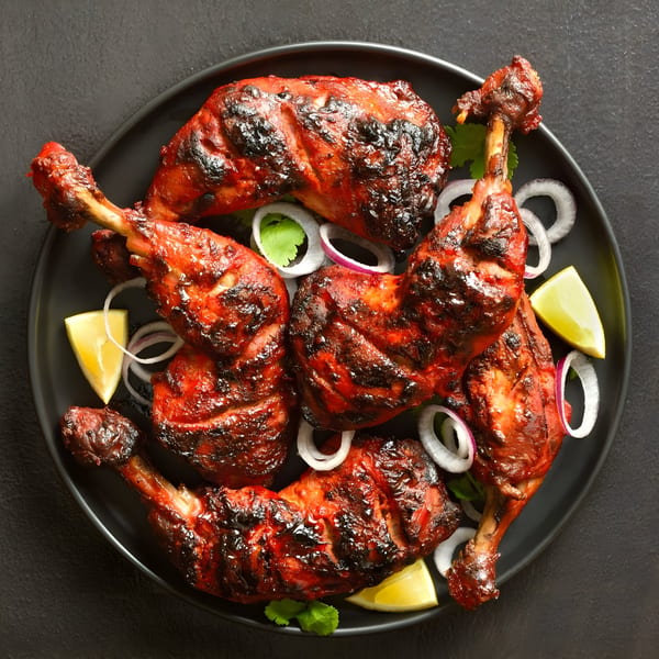 Masthi Indian Cuisine's Tandoori chicken drumsticks and thighs, garnished with onion rings, cilantro, and lime wedges.