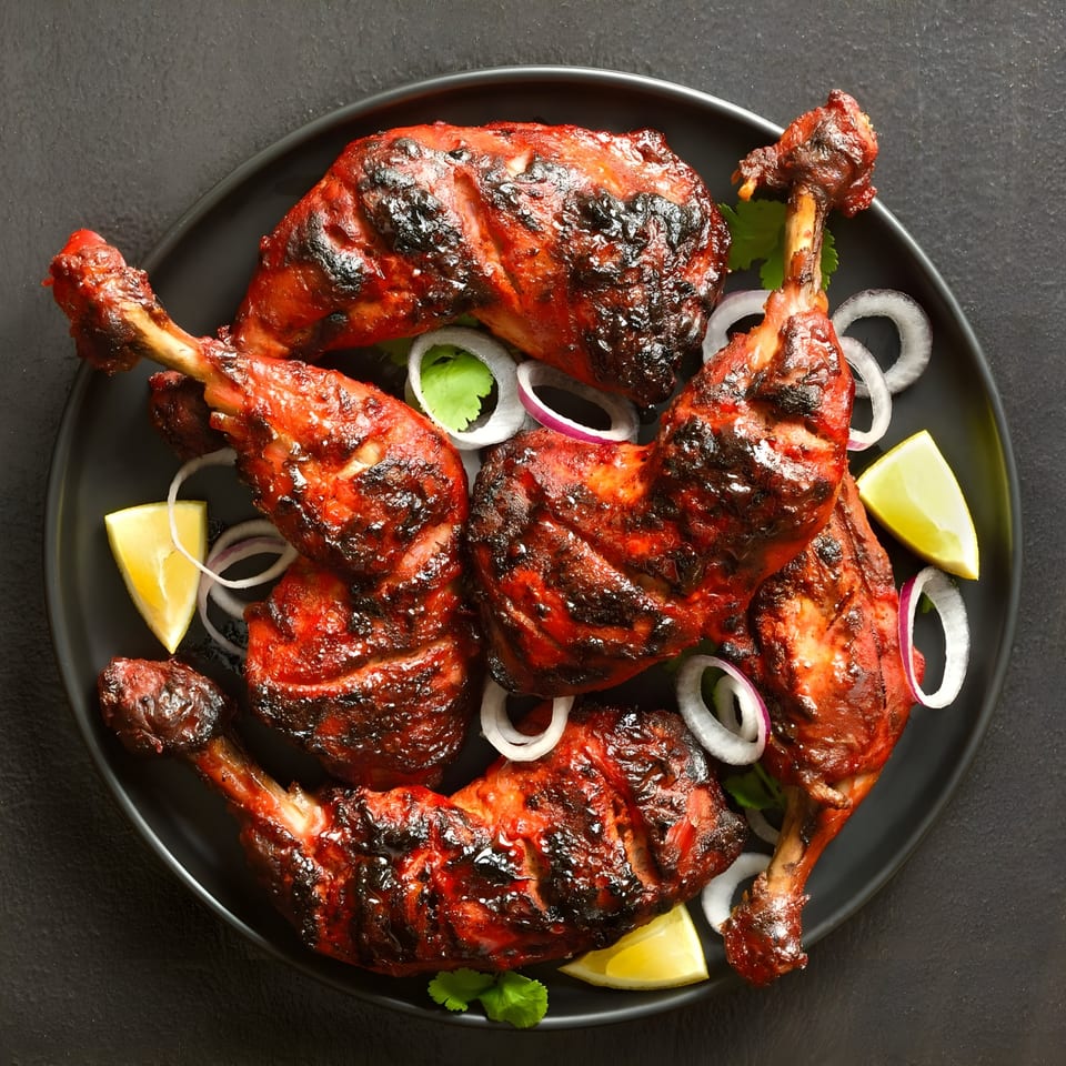 Masthi Indian Cuisine's Tandoori chicken drumsticks and thighs, garnished with onion rings, cilantro, and lime wedges.