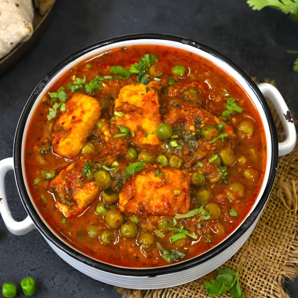 A white bowl filled with vibrant red Indian Mutter Paneer curry, garnished with fresh cilantro.
