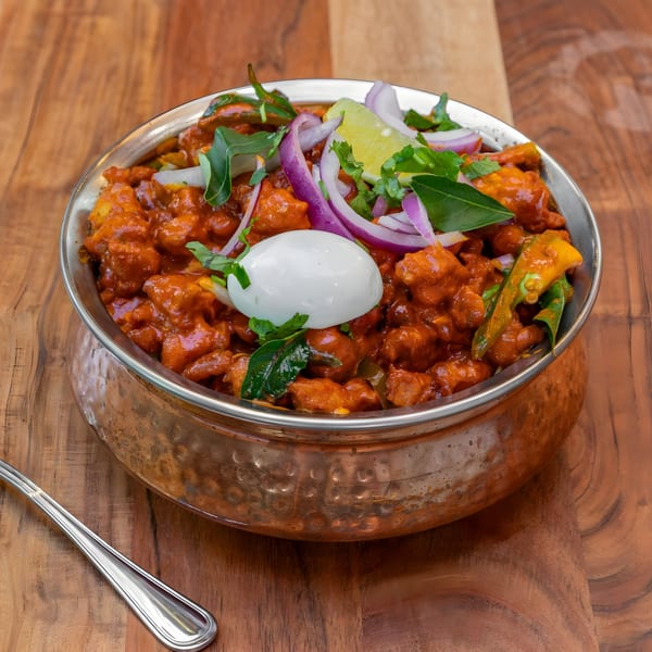 Masthi Indian Cuisine's chicken 65, garnished with onions, lime, and a boiled egg, in a copper bowl.